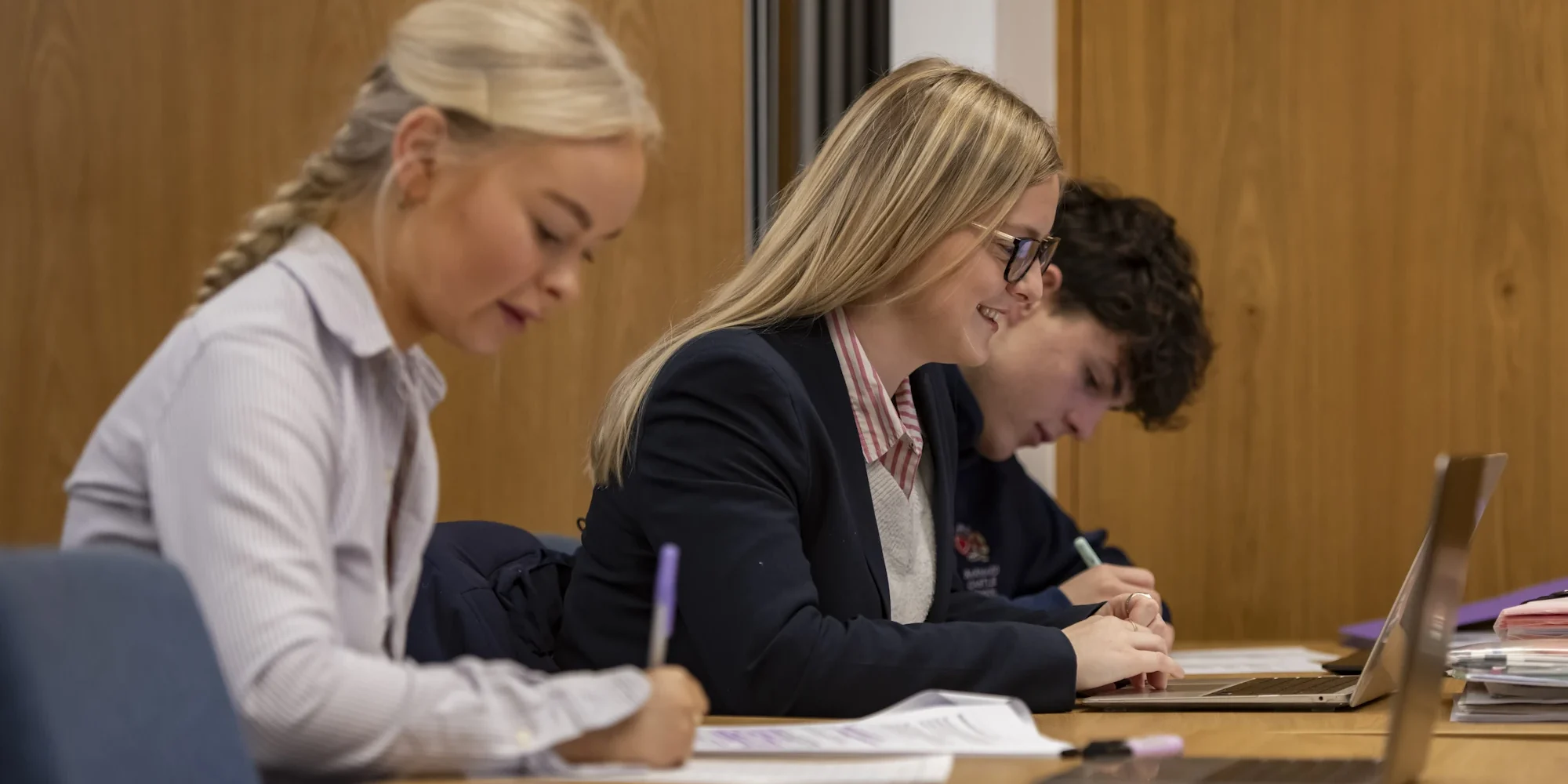 Barnard Castle School Sixth Formers working at a desk with their laptops and writing notes in a classroom.