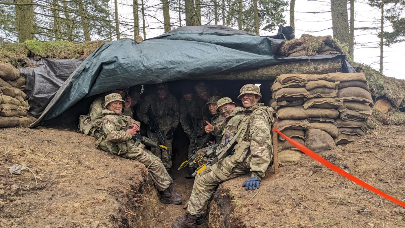 A group of Barnard Castle School students in army gear smiling at the camera in a bunker.