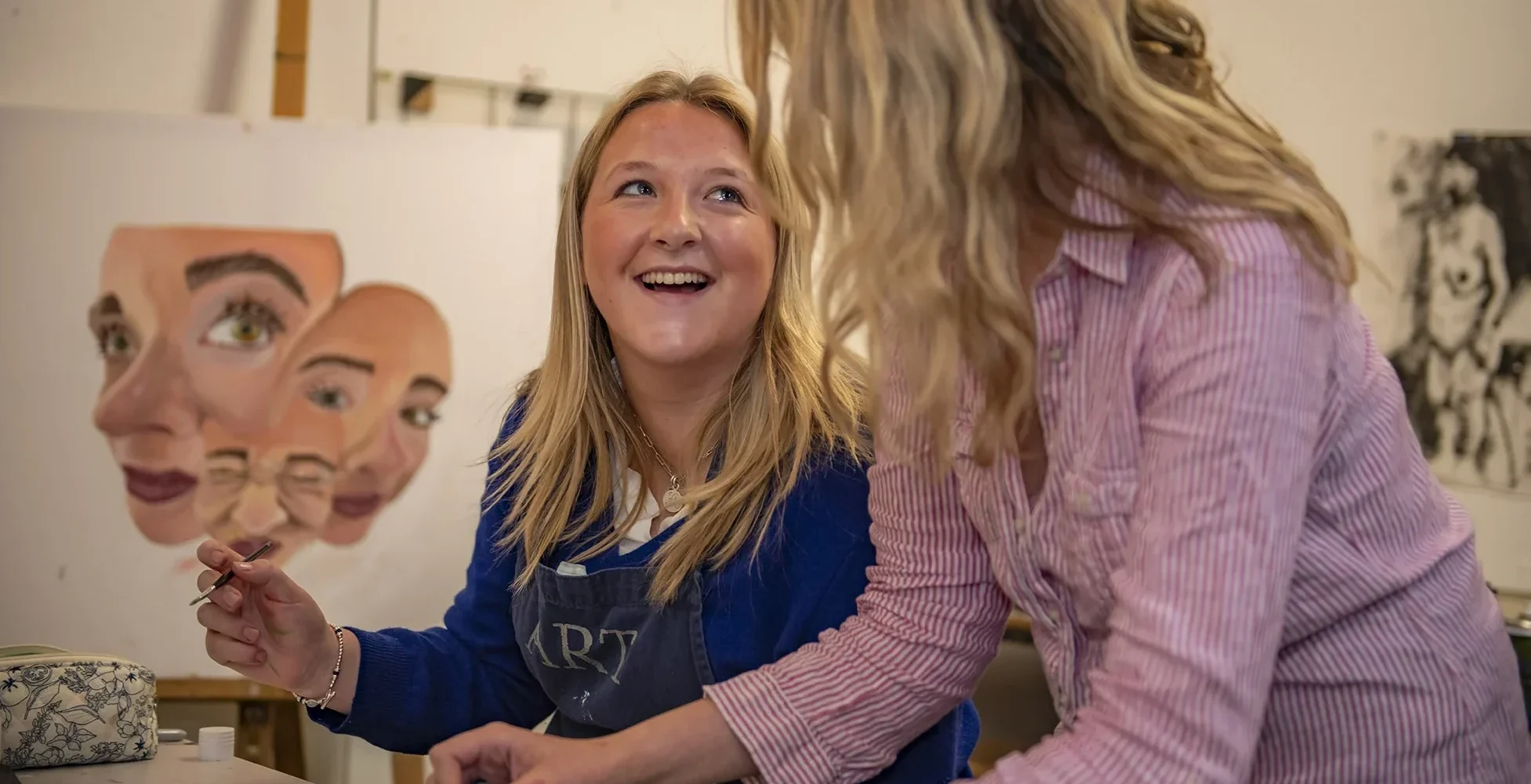 A Barnard Castle School art student and teacher laugh together while painting on paper, enjoying a creative and joyful moment.