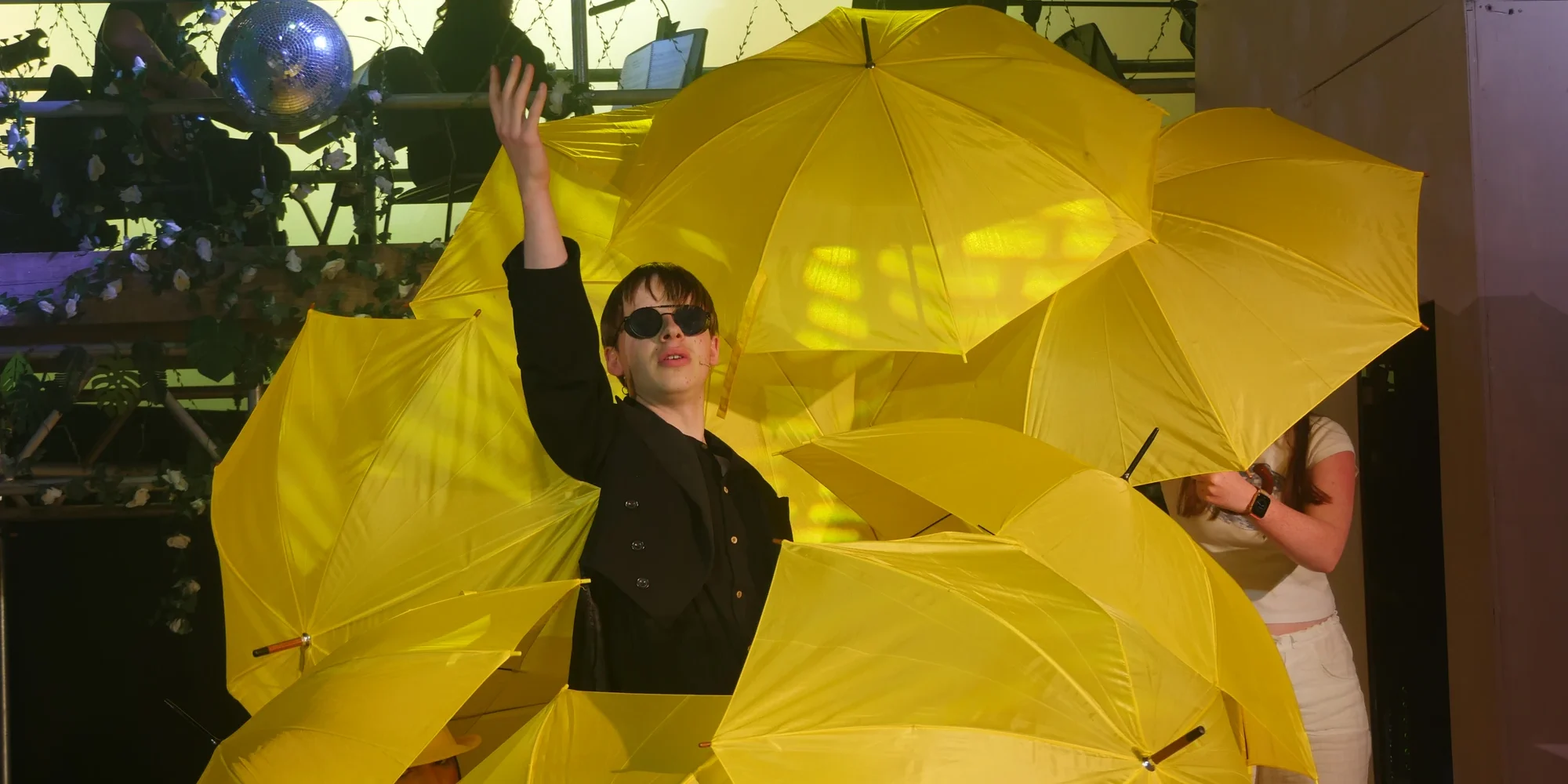 Senior school student performing on stage surrounded by yellow umbrellas.