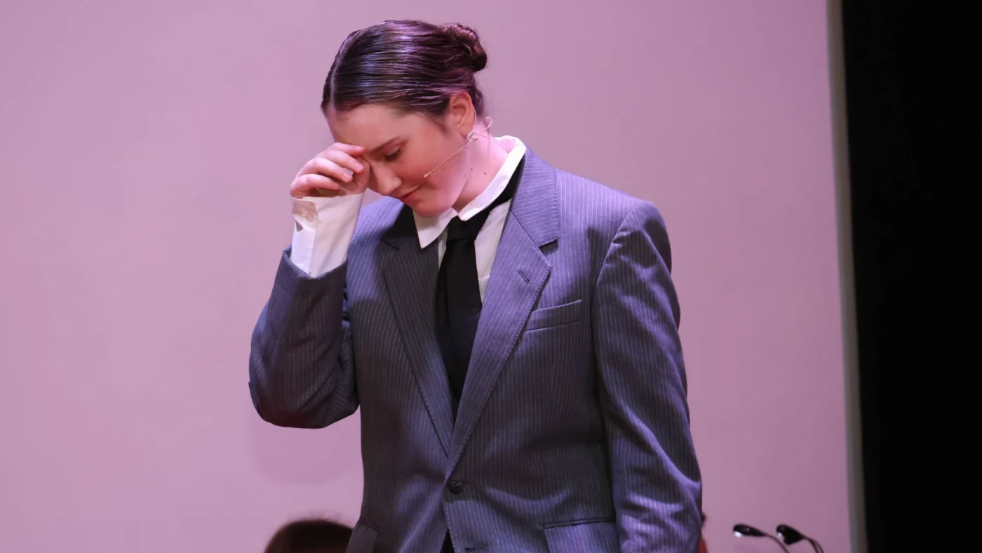 A Barney student in a suit and tie acts on stage.