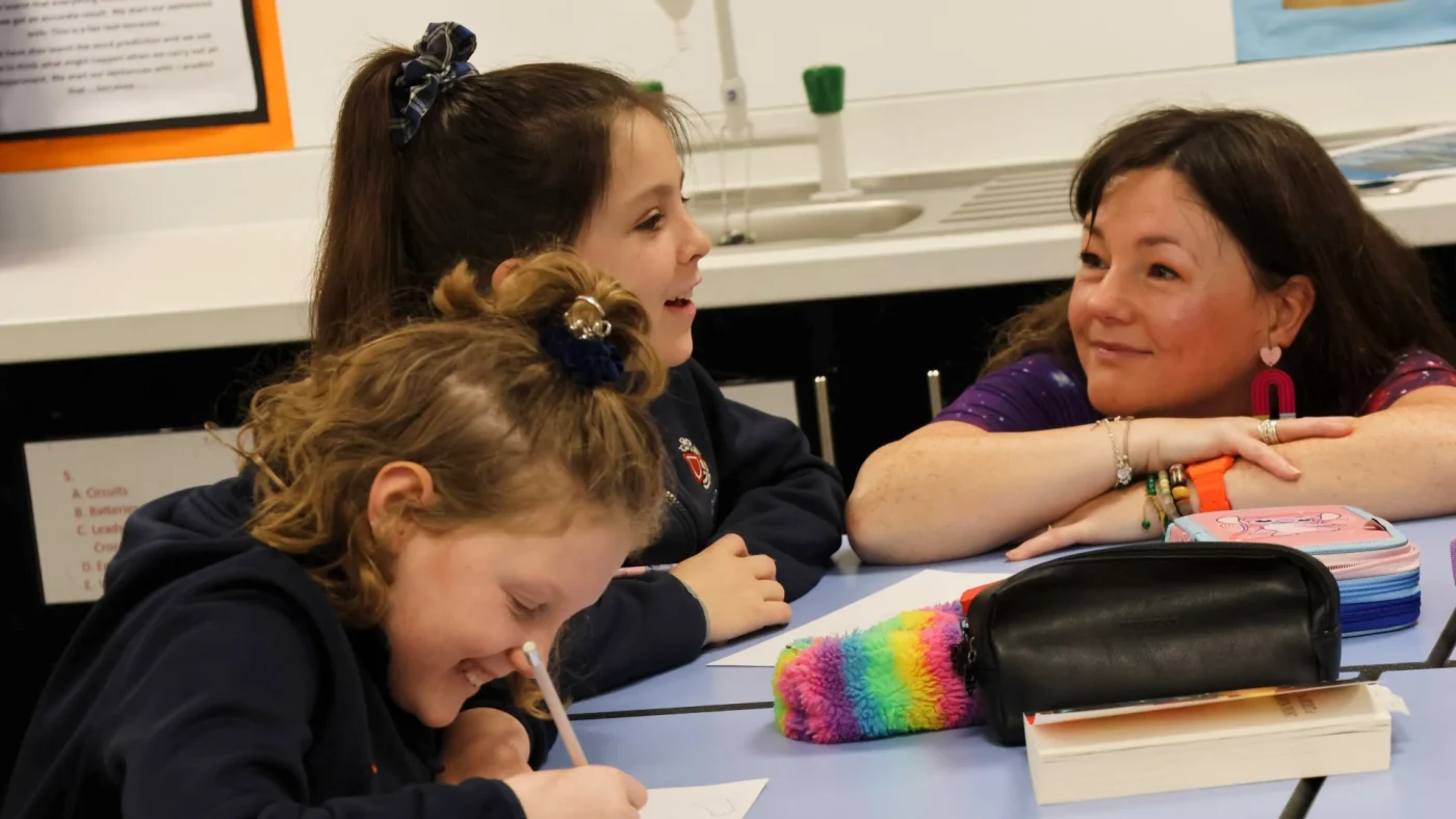 Lisette Auton sits with Barney Prep School students as they write.